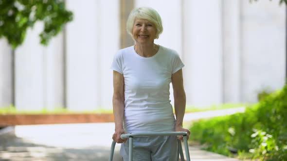 Cheerful Senior Woman With Walking Frame Looking at Camera Outdoors, Rehab alt