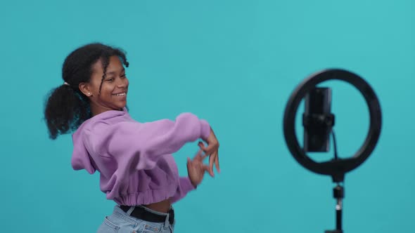 Pretty African Girl Dances to the Music on a Blue Background Young Influencer Takes a Selfie Video alt