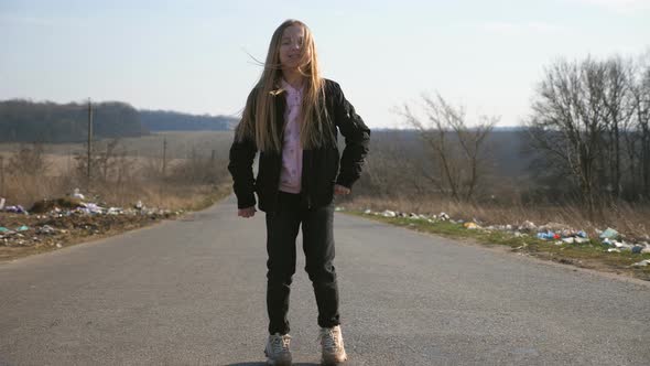 Cheerful Female Child with Long Blonde Hair Dances Funny on the Road at Countryside alt