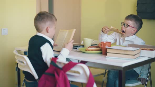 Schoolkid Eats Pizza and Friend Reads Textbook at Table alt