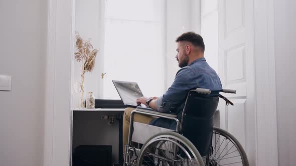 Bearded Guy which Sitting in Wheelchair and Remotely Working on Computer  alt