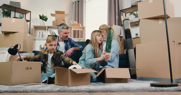 Family with Two Kids Sitting on the Floor Among Cardboard Boxes in Relocation Day alt