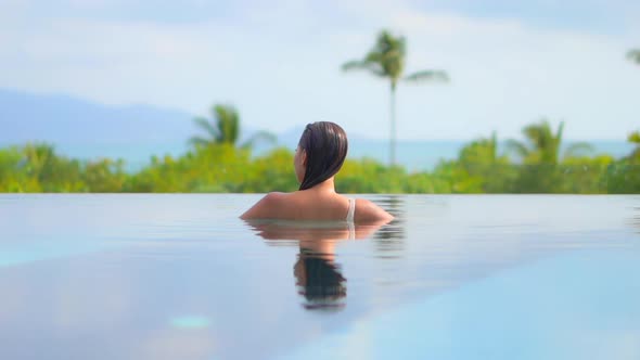 An unrecognizable woman inside infinity pool looking at amazing tropical greenery on hills backgroun alt