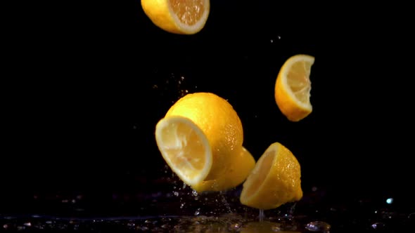 Super Slow Motion Pieces of Fresh Lemon Fall on the Table with Splashes of Water alt