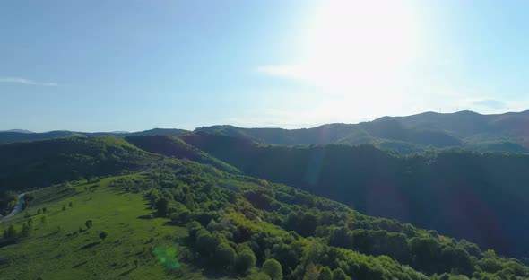 Aerial Shot of Woods, Green Hills and Meadows Under Bright Shining Sun and Blue Sky alt