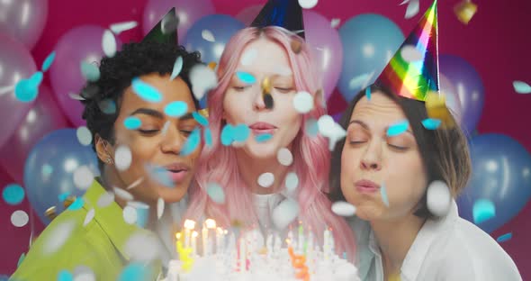 Three Friendly Millennial Women Blowing Candles on Birthday Cake Party with Confetti Rain alt