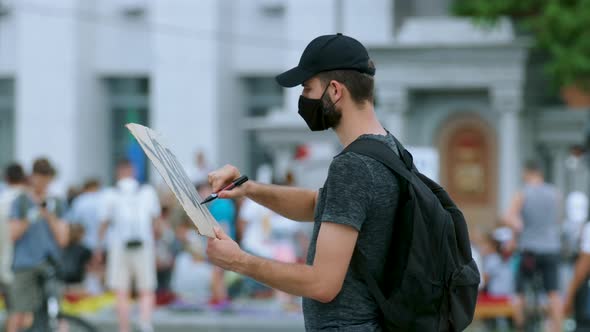 Masked riot activist man drawing poster sign, poster banner. Rebel on rally. alt