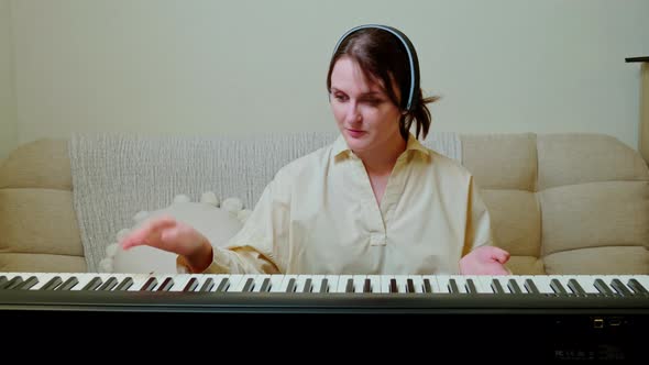 Woman musician with piano looking at video camera at home on sofa in living room alt