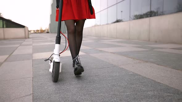 Young Woman Walks with Electric Scooter alt