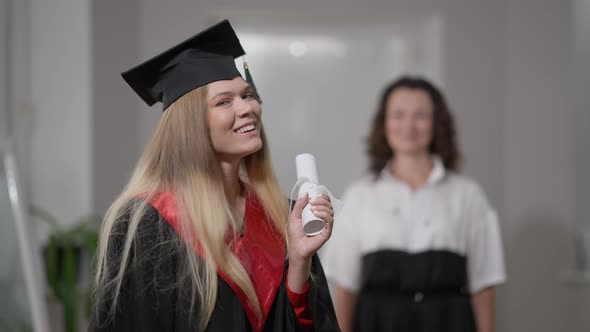 Happy Excited Graduate Posing with Rolled Diploma Looking Back at Blurred Woman alt