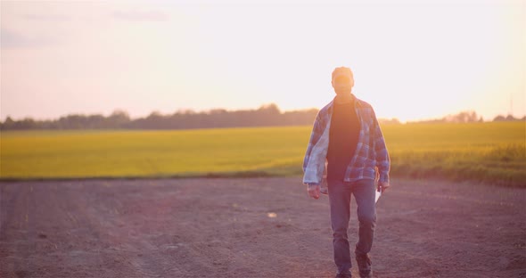 Agriculture - Farmer Walking on Field Examining Crops at Farm at Dusk alt