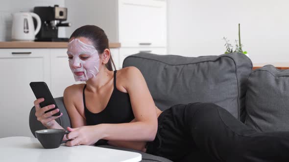 Young Millennial Woman at Home Applying Cloth Mask on Face and Using Phone. Wellness Relaxing Time  alt