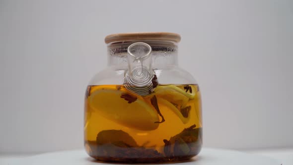 A transparent glass teapot filled with hot citrus tea revolves.