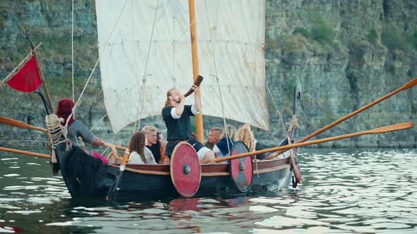 Vikings Sail on an Old Ship with a Raised Sail on a Calm River alt