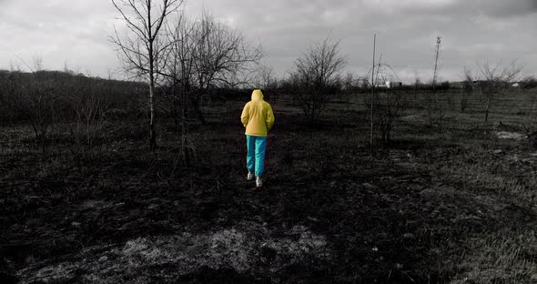 Teenage Homeless Girl in Colorful Ukrainian Clothes Walks on a Burnt Field alt