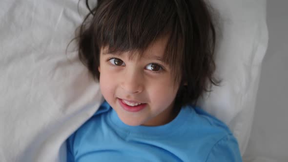 Boy Child in a Blue Tshirt Lies on a White Bed