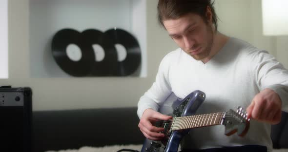 Creative Musician in a Gray Jumper Tunes a Blue Electric Guitar