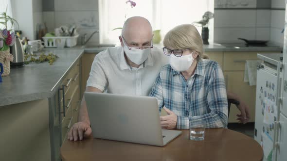 Man And Woman In Medical Masks Sitting At Laptop. alt