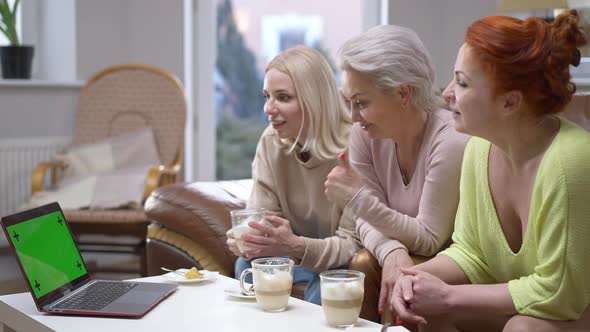 Three Positive Women Sitting on Couch Waving at Laptop with Chromakey Green Screen Smiling alt