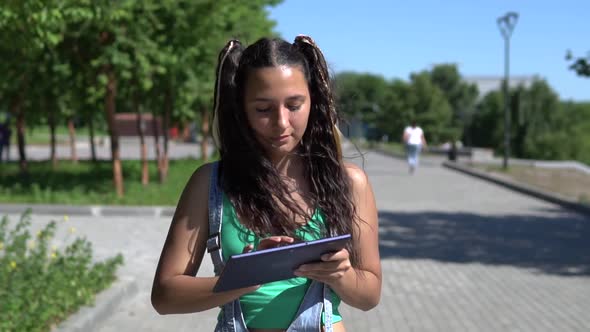 A Beautiful Girl is Walking in the Park Using a Tablet alt