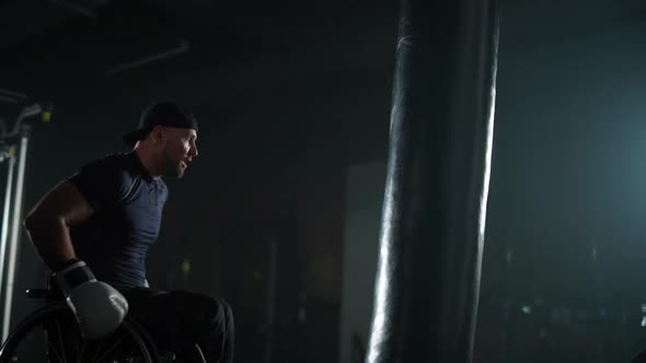 Disabled Man in Wheelchair Trains Punches on a Punching Bag Training in the Boxing Gym alt