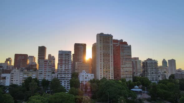 Aerial rising over park at sunset with sun setting behind buildings in Belgrano neighborhood, Buenos alt