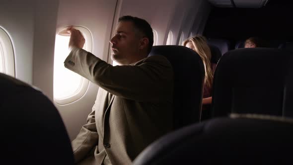 Man on airplane closes window and takes a rest