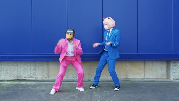 Couple in business suits and animal masks dancing in front of wall alt