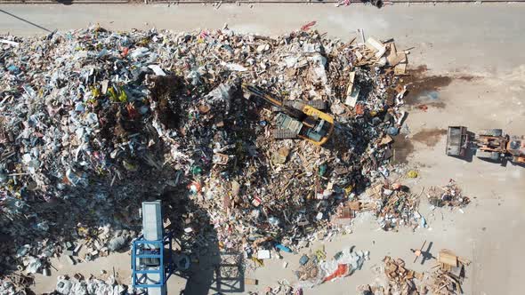 Excavator shovels out a pile of rubbish at a landfill alt