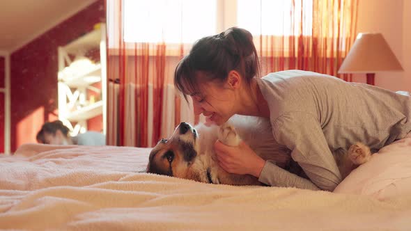 Smiling Woman with Dog in Bed at Home, Hugging Funny Yawning Dog Welsh Corgi alt