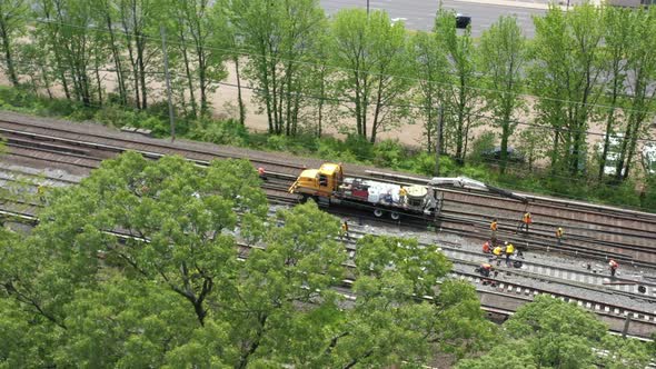 an aerial view over trees looking at men fixing train tracks on a sunny day. The camera focuses on a alt