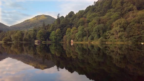 Mirror reflection of hills, woods and boathouses on Ullswater lake alt