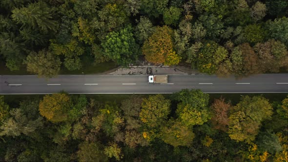 A fast driving lorry at a straight road in a autumn colored forest street, filmed from above by a dr alt