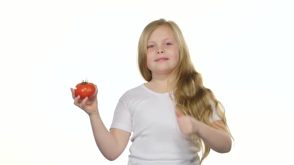 Kid Girl Looks at a Tomato, Admires It and Shows a Thumbs Up. White Background alt