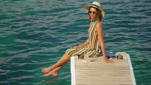 A woman with a glass of white wine on a dock over the Mediterranean Sea in Italy, Europe. alt