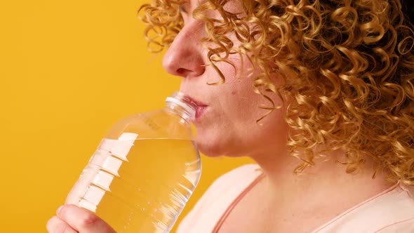 Happy Girl Holds Bottle of Detox Drink Poses Against Yellow Background