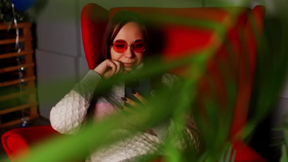 Woman in Stylish Sunglasses Sitting in Armchair with Smartphone alt