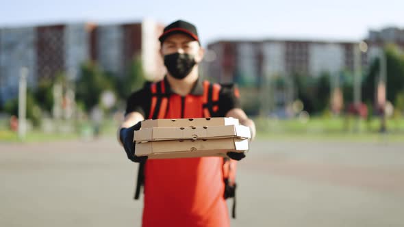Portrait of Courier Delivery Man Wearing Face Mask With Red Backpack Holding Pizza in Carton Boxes alt