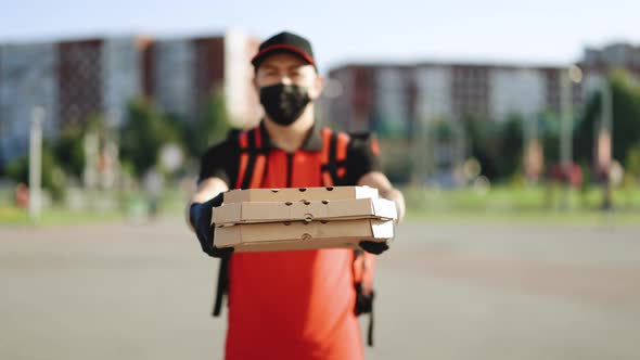 Portrait of Courier Delivery Man Wearing Face Mask With Red Backpack Holding Pizza in Carton Boxes