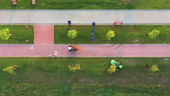 Top drone view of lawn mowers on tractors mowing the lawn in a city park at dawn