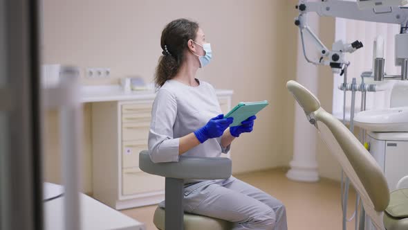 Expert Female Orthodontist with Tablet Spinning on Chair in Dentist Office Looking at Equipment alt