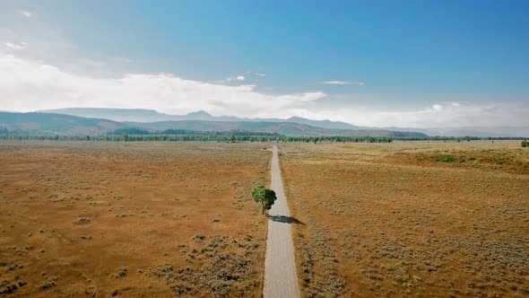 Drone flies over a long road that runs across prairie to the horizon near Mormon Row, Wyoming, USA alt