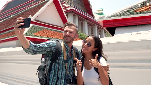 Lovely young tourist couple taking selfie with smartphone at Thai temple