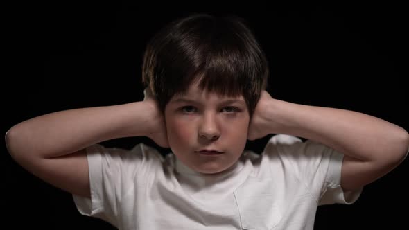 Serious Sad Boy Looking at Camera Covering Ears with Hands alt