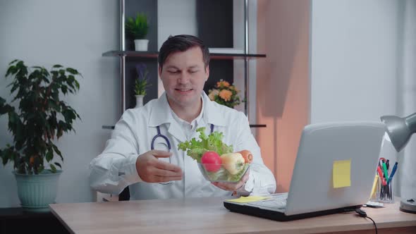 Portrait of a Male Nutritionist Holding a Plate of Vegetables While Sitting at the Table