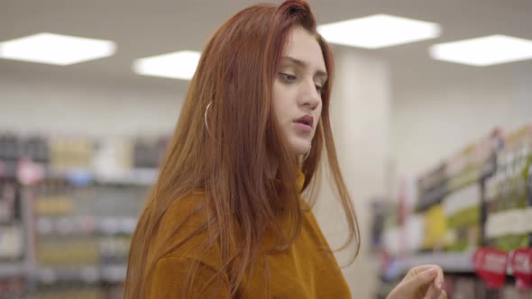 Portrait of Focused Redhead Caucasian Woman with Green Eyes Shopping in Wine Shop. Confident alt