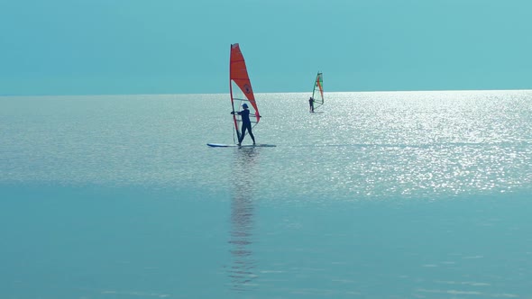 Silhouette Windsurfer Sailing on Windsurf Board on Sea at a Beautiful Sunset Sky on Background alt