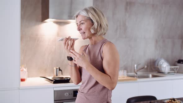 Mature woman using smartphone at breakfast table alt