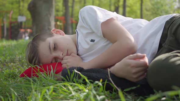 Portrait of a Cute Boy Lying on Green Grass in Spring Park. Outdoor Recreation alt