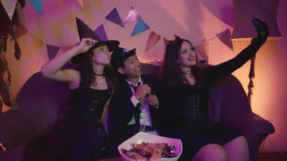 A Group of Friends are Sitting at a Table in Creepy Costumes Taking Pictures on Their Phone and alt